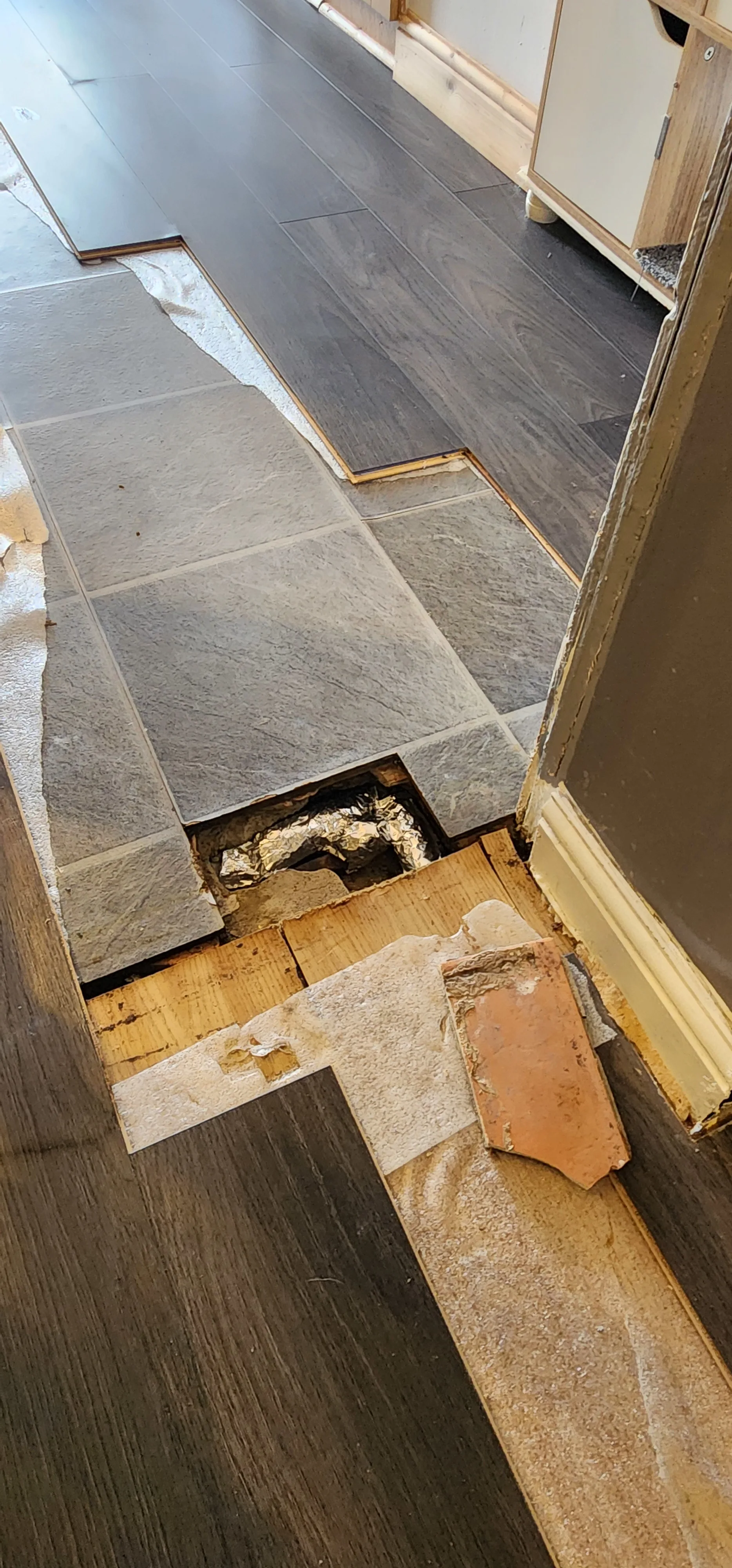 Lifted dark flooring and a focused opening in the tiled kitchen floor
