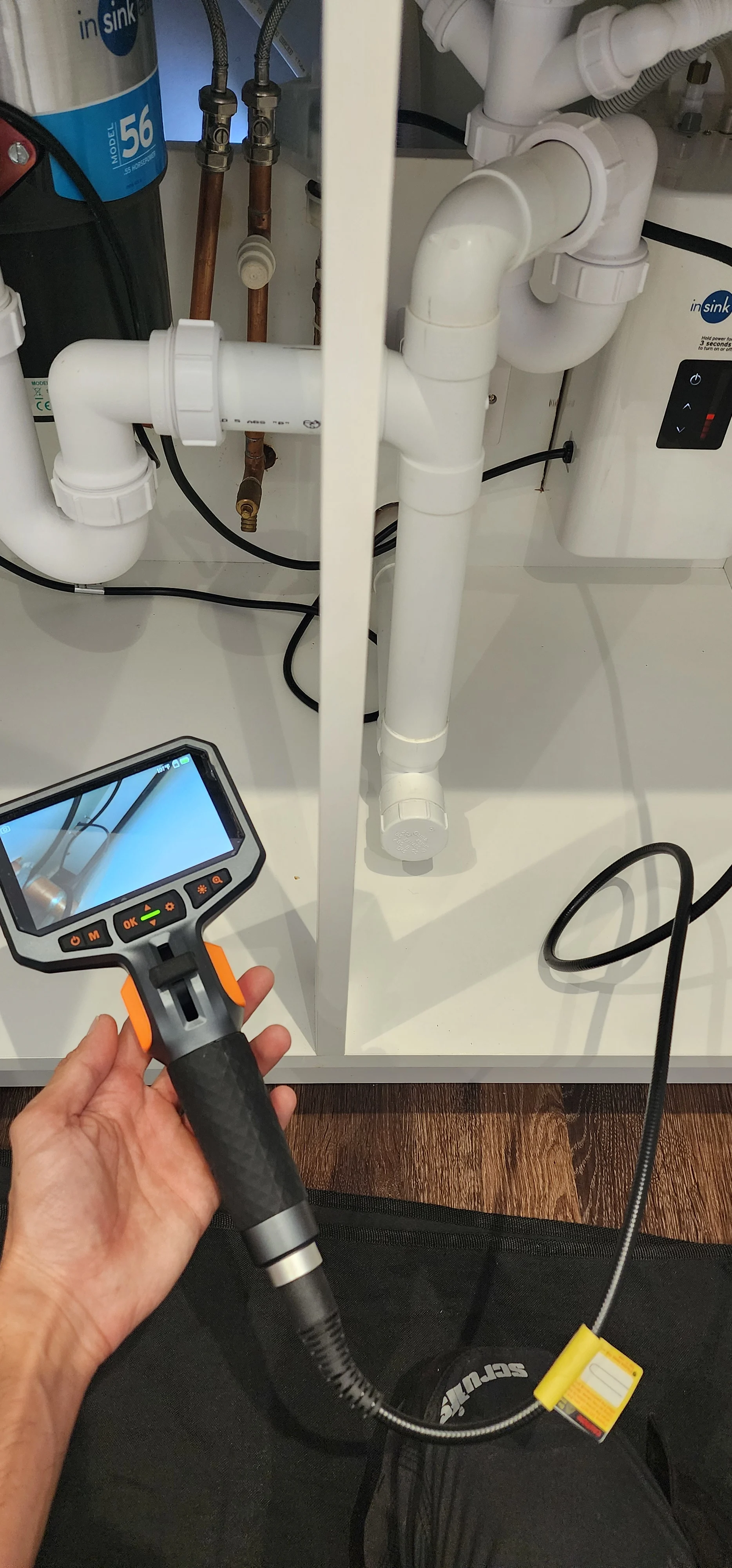 Endoscopic camera held in front of sink pipework and white waste fittings